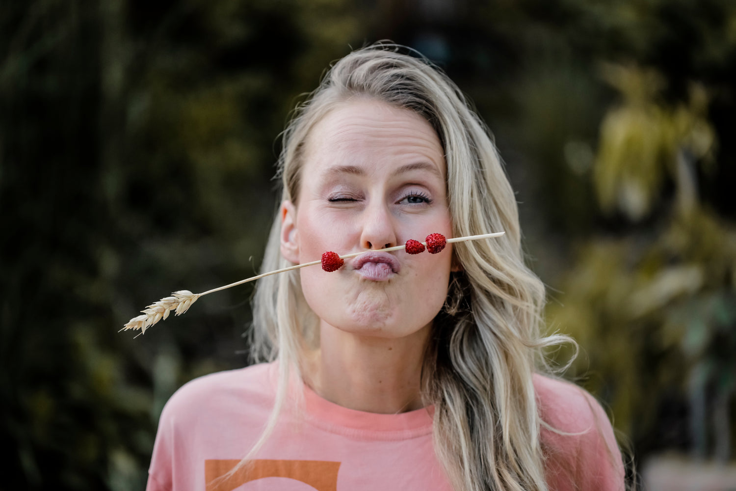 Founder Kira squinting at the camera holding a straw with strawberries between her lip and nose
