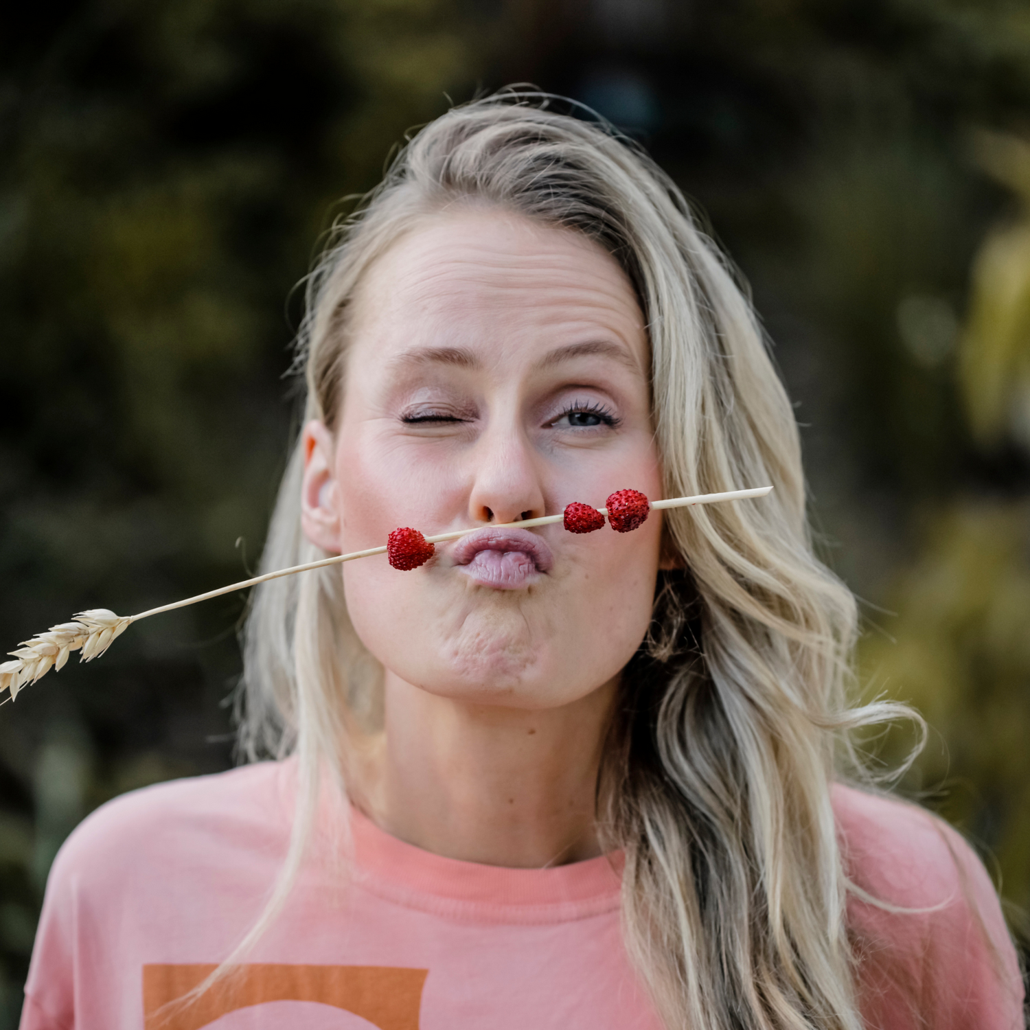 Founder Kira squinting at the camera holding a straw with strawberries between her lip and nose
