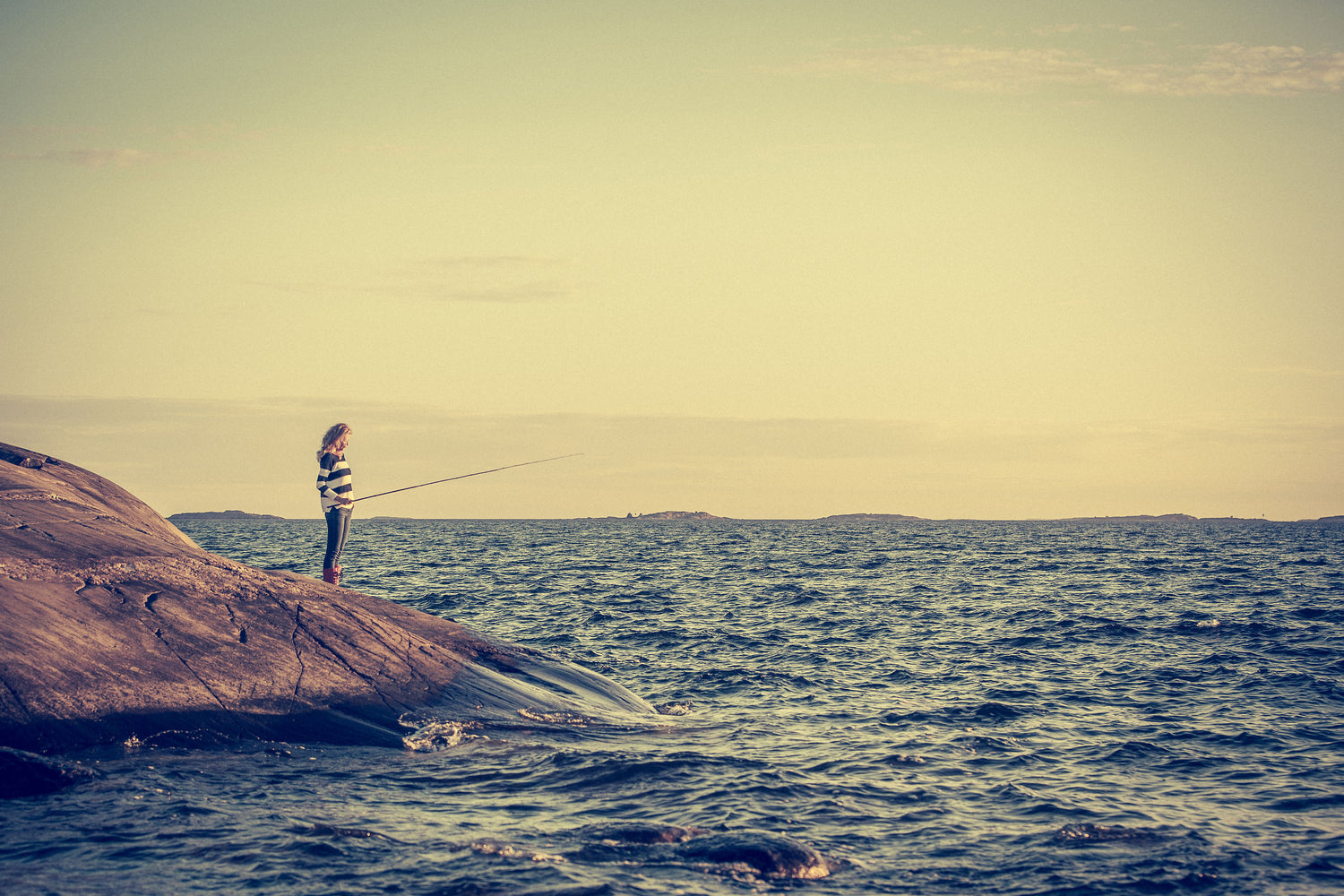 Kira fishing on a rock surrounded by the ocean