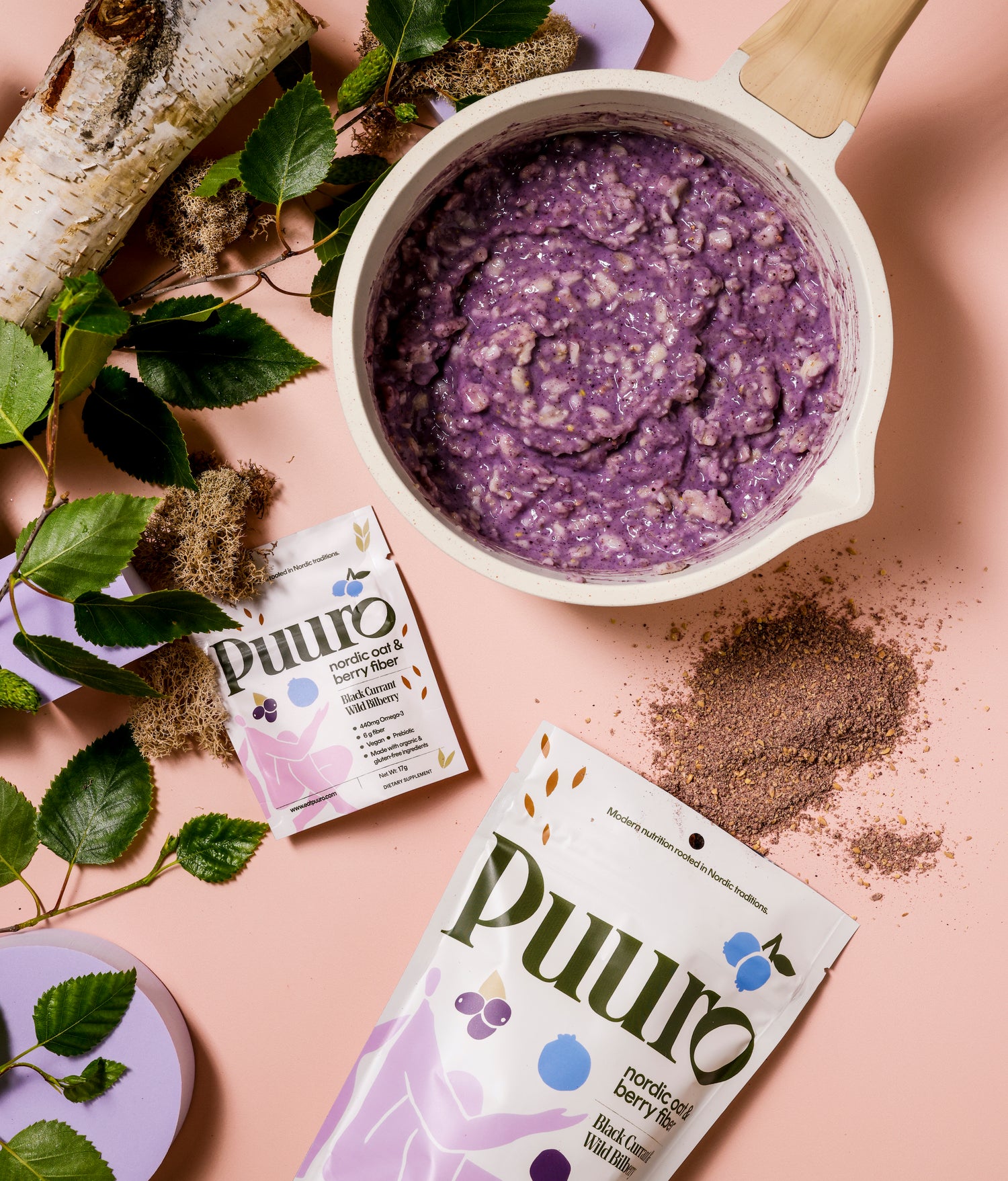 A Puuro fiber pouch opened on a table, with insides scattered, laying beside a pot of cooked purple oatmeal.