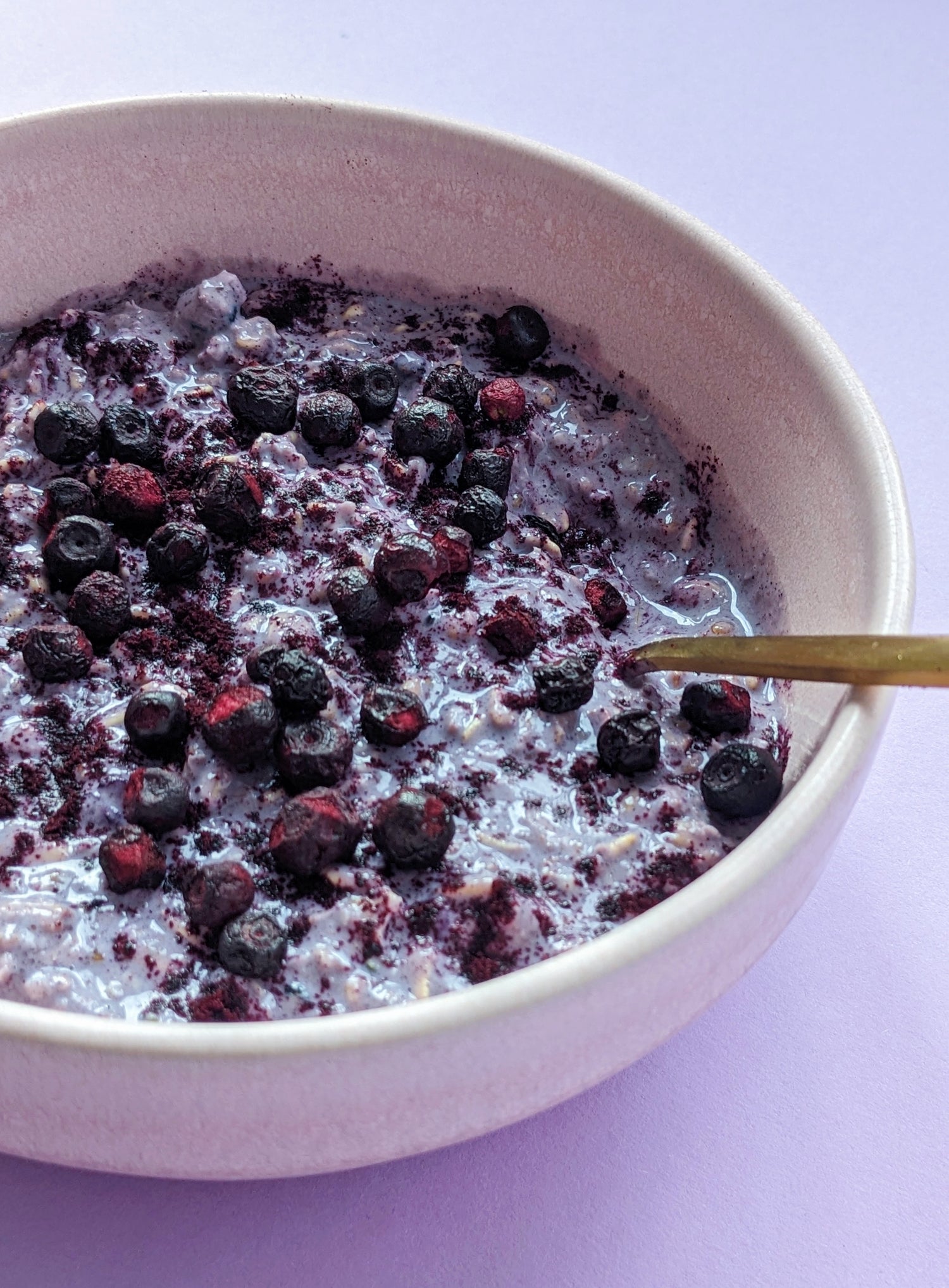 Puuro wild bilberry & black currant Nordic oats in a bowl with a spoon with blueberries sprinkled on top